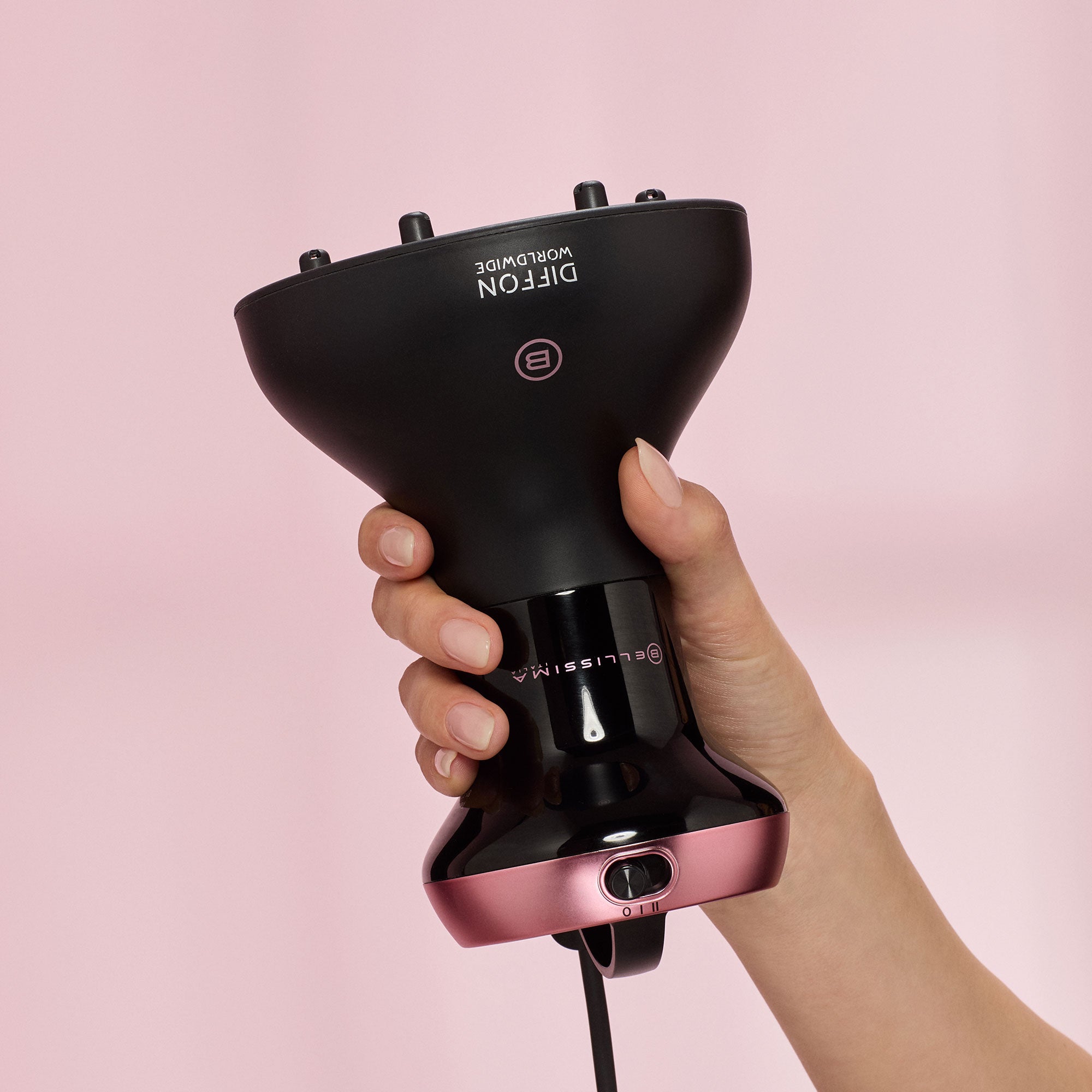 Hand holding a black and pink Diffon World wide Curly Hair dryer against a pink background
